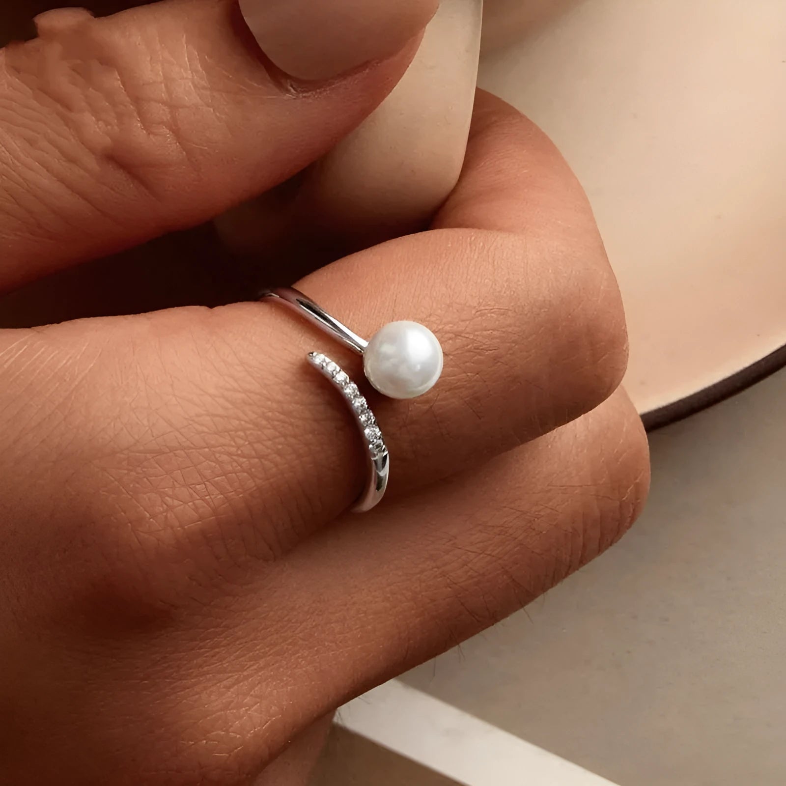 Silver adjustable open ring with white shell pearls on a white background.