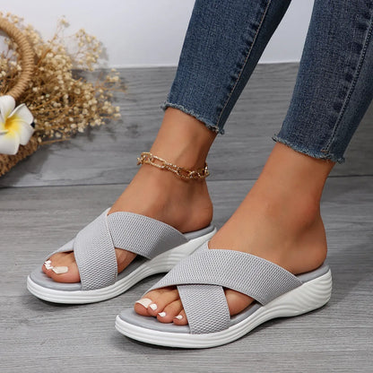 Women's black wedge-heel slippers with peep toe and cross-strap design on a thick rubber sole.