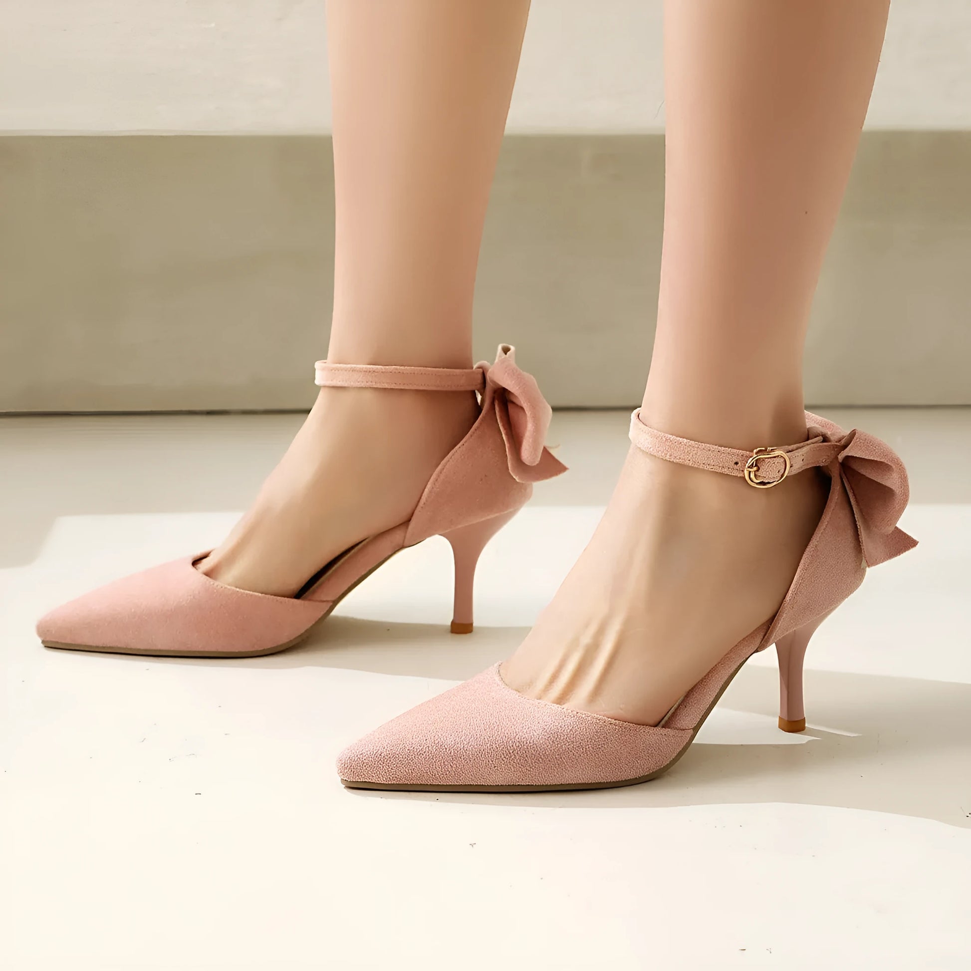 Black stiletto high heels with pointed toe, bowknot detail, and buckle closure on suede upper