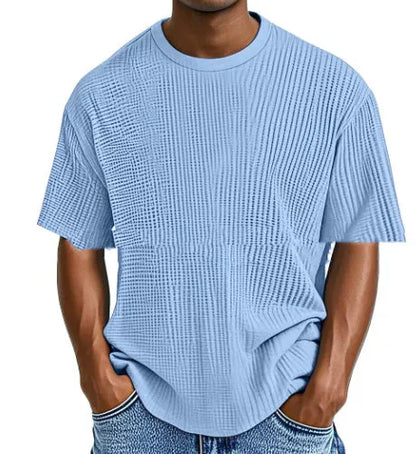 Man wearing a light blue waffle-textured cotton blend short sleeve t-shirt, casual pullover style.
