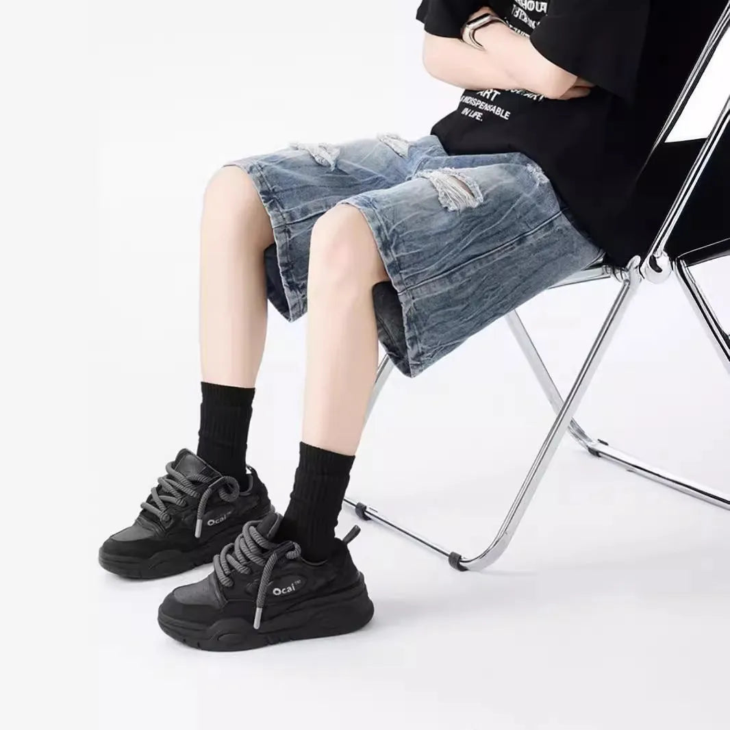 Man wearing loose fit black ripped denim shorts with distressed detailing and a washed vintage finish.