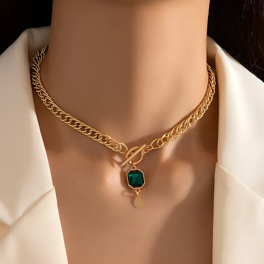 Gold geometric pendant necklace with emerald green zircon on a textured Cuban link chain.