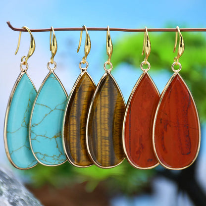 Close-up of long, polished tigereye stone drop earrings with a fishhook clasp on a neutral background.