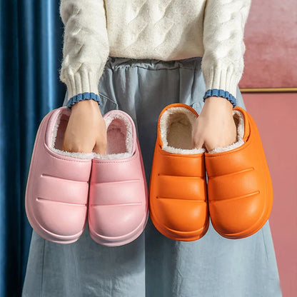 A pair of green waterproof EVA slippers with a plush lining and textured non-slip sole on a wooden floor.
